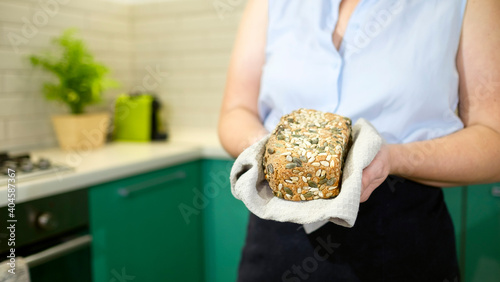 Housewife holds sourdough bread with sunflower and pumpkin seeds in hands in her kitchen