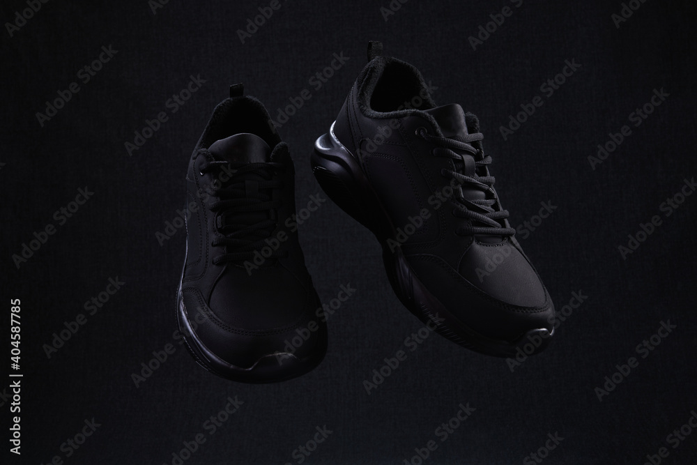 Pair of fashion black unbranded sneakers flying on dark background. Black sport running shoes levitate in air.