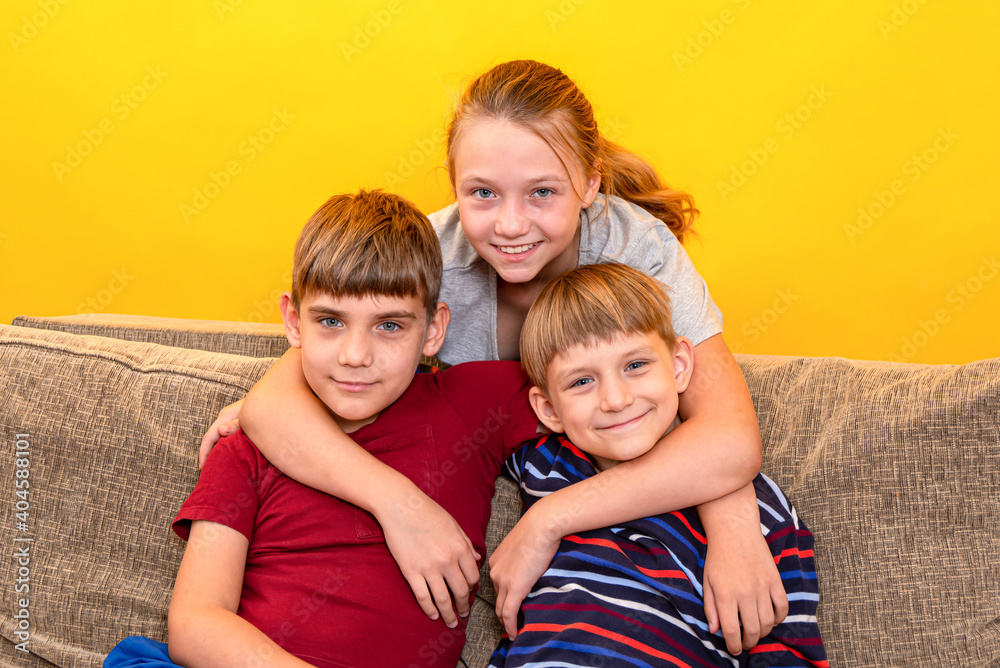 The friendly family is embracing and sitting on the sofa near the orange background.