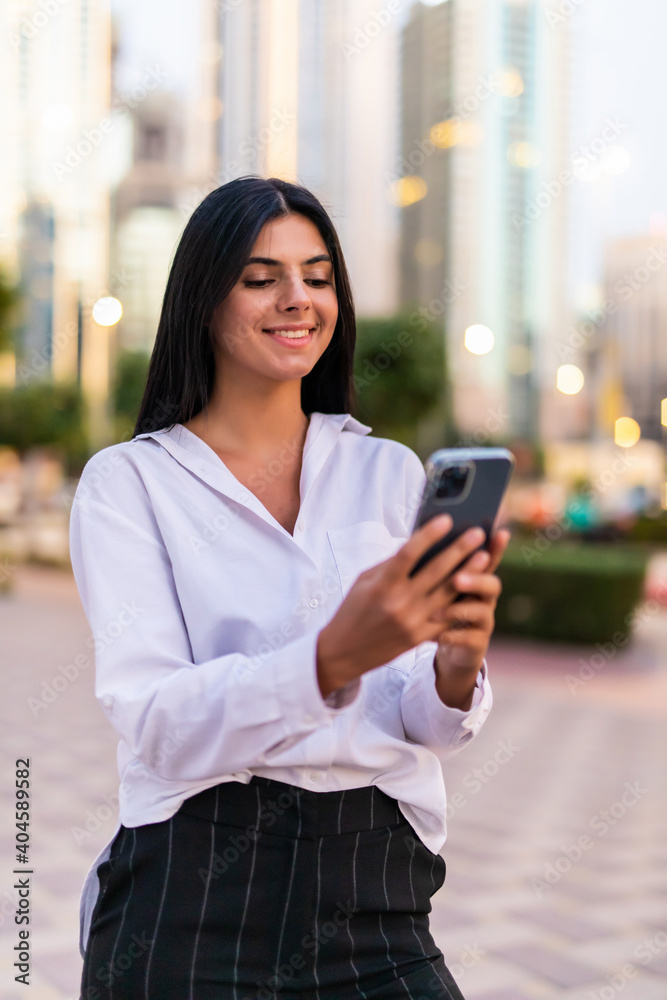 Fototapeta premium Business woman uses smartphone outdoors in big city with skyscrapers in the background.