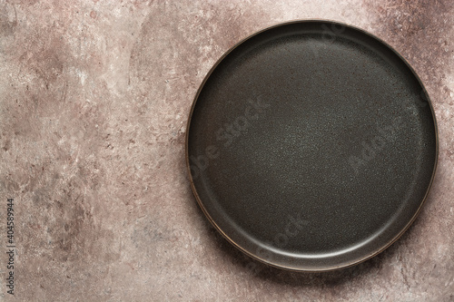 Empty craft plate in gray-brown on beige grunge background. Top view, flat lay.