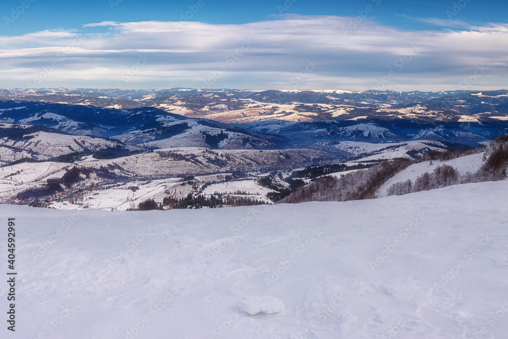 Scenic winter landscape, amazing panoramic mountain view of ridges and peaks of the Carpathian mountains and blue sky with clouds, outdoor travel background, Zakarpattia, Ukraine