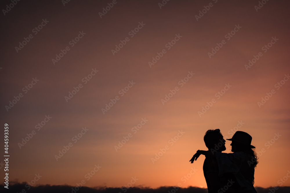 silhouette of a couple that looks at each other and hugs against the light in a sunset. Classic romantic image of a couple in love against a sunset background. Copy space Valentine's concept