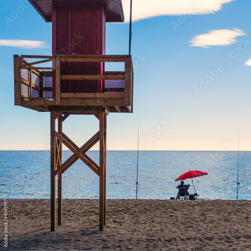 Pescador en la orilla de la playa junto a una torre de vigilancis de playas en Mijas