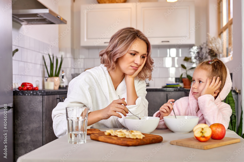 mother and child girl sit dont' want to eat in the morning, they have no appetite, want to sleep. in the kitchen mother and child girl sit dont' want to eat in the morning, they have no appetite, want to sleep. in the kitchen