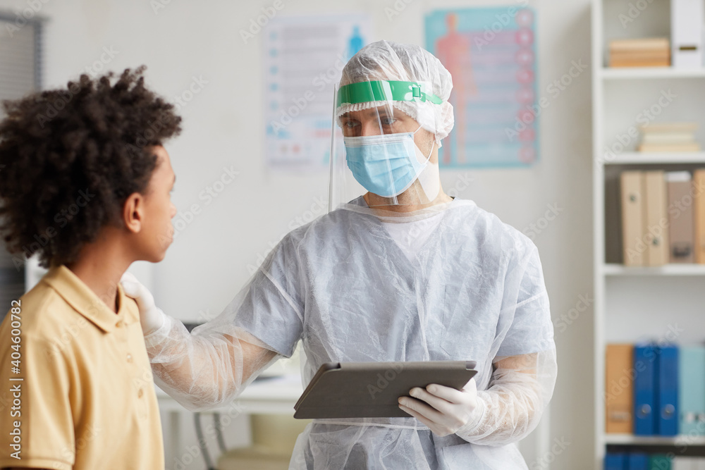 Obraz premium Portrait of doctor wearing full protective gear talking to African-American boy during consultation in clinic, copy space