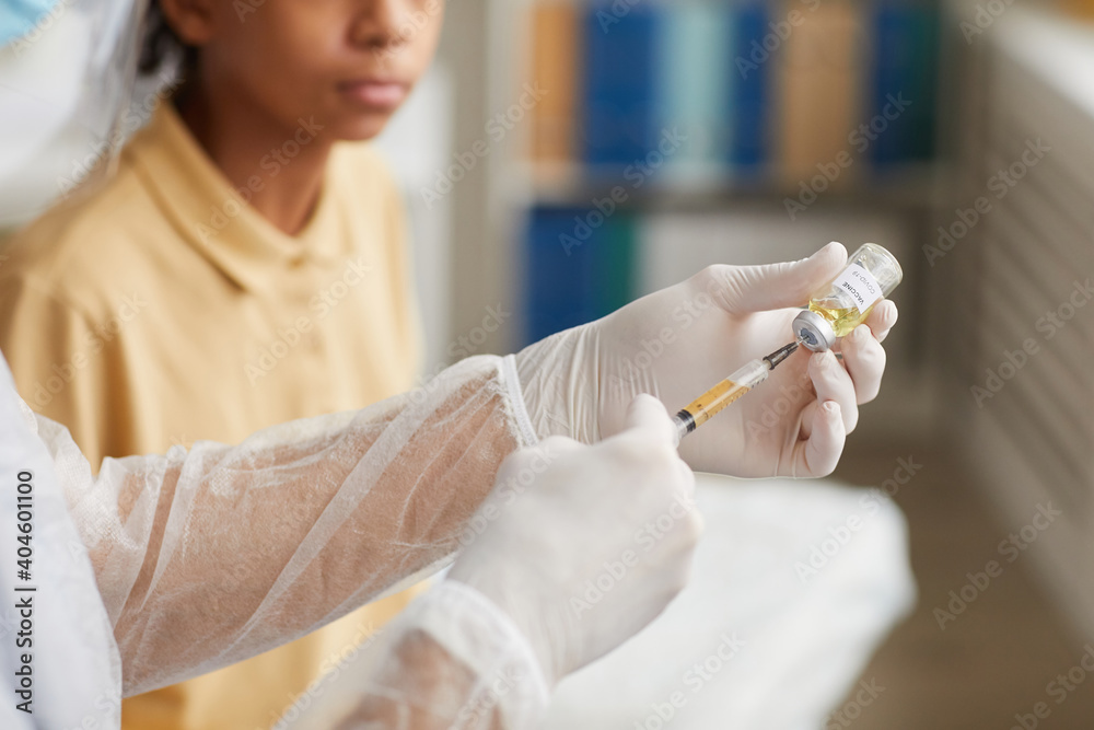 Close up of nurse drawing medicine into syringe while vaccinating African-American boy in clinic, copy space Close up of nurse drawing medicine into syringe while vaccinating African-American boy in clinic, copy space