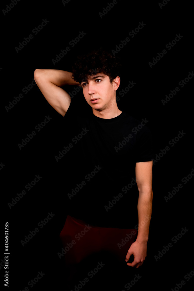 Attractive young man with curly hair posing on black studio background