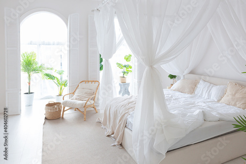 Cozy interior of a bright Balinese-style apartment with white walls, bamboo furniture. bed room with night lights, bed with balanchin and large windows