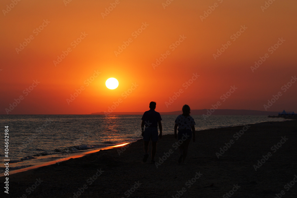 Silhouette Middle age couple walks along the coast at sunset