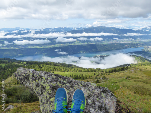 A pair of shoes resting of the rock with a view on the Millstaettersee from Granattor in Austrian Alps. The distant lake is surrounded by high mountains. There are few clouds above the region. Mystery photo