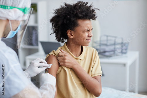 Portrait of unrecognizable male nurse vaccinating African-American boy squinting in fear , copy space