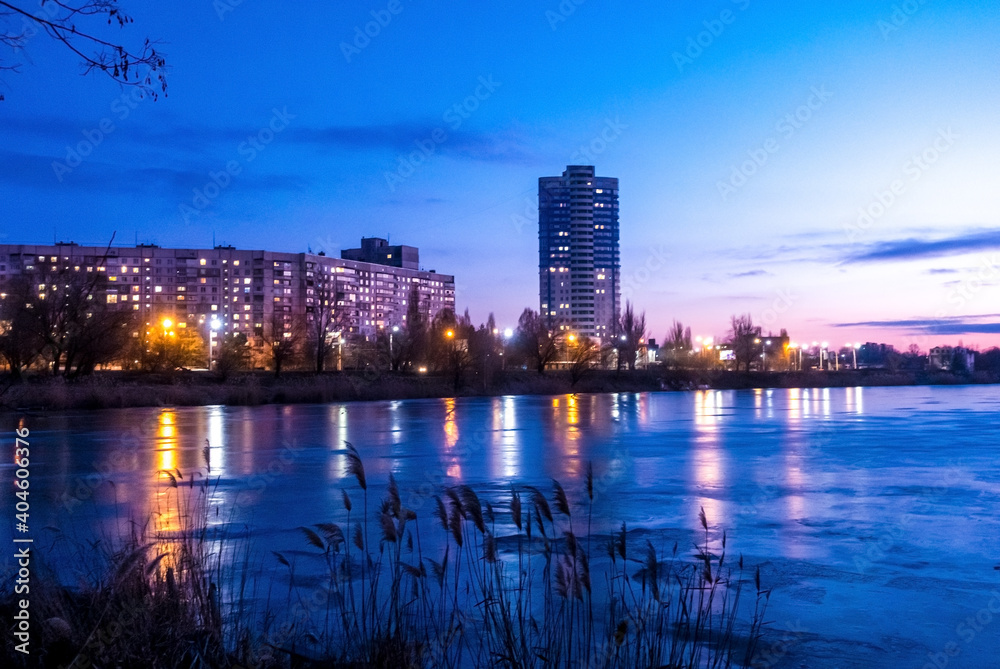 Evening city donwtown landscape with sunset, electric lights and frozen lake. Kharkiv, Ukraine
