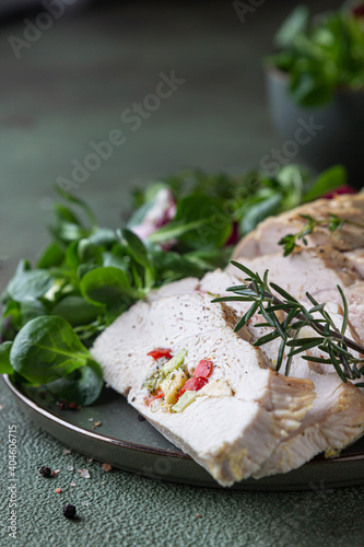 Turkey breast stuffed with vegetables and cheese served with green mix salad and aromatic herbs, green stone background.
