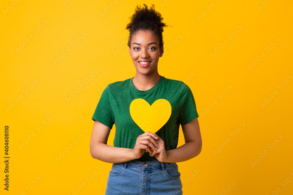 Smiling black woman holding yellow heart and looking at camera Smiling black woman holding yellow heart and looking at camera