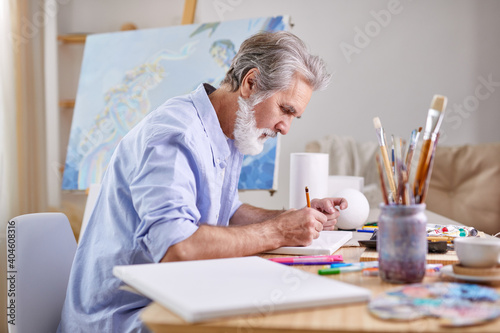 painter is drawing at home using pencil, concentrated on work, wearing blue shirt.