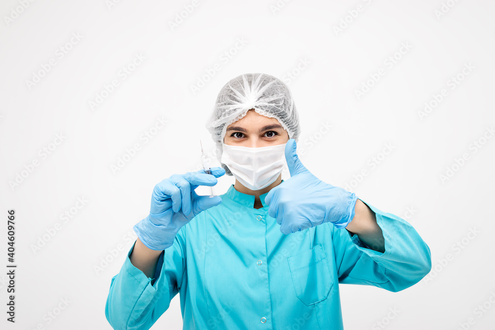Positive medical worker in protective clothing,gloves and mask holding a syringe and showing the thumb up sign.Medicine and healthcare concept.Coronavirus vaccination concept. Positive medical worker in protective clothing,gloves and mask holding a syringe and showing the thumb up sign.Medicine and healthcare concept.Coronavirus vaccination concept.