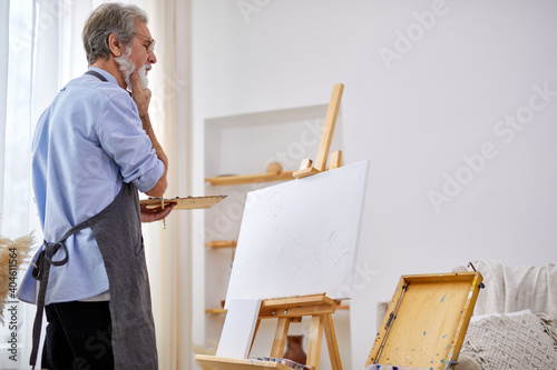 thoughtful artist man standing behind canvas on easel, in contemplation, think what to draw