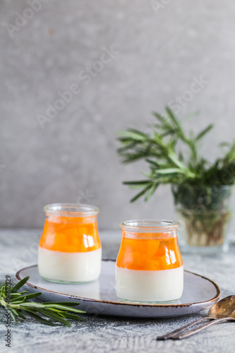 homemade panna cotta with slices of peach and peach jelly in glass jars on a gray concrete background