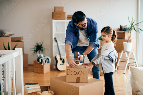 Happy little girl and her father packing cardboard boxes while relocating into a new home.