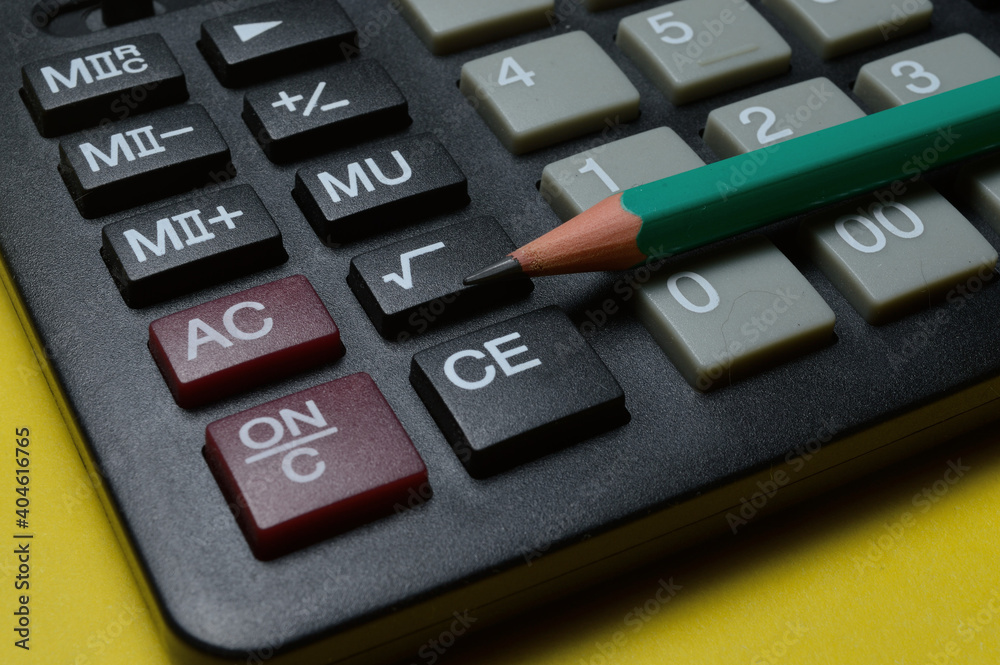 calculator and pencil lie on a yellow background. close-up. calculator and pencil lie on a yellow background. close-up.