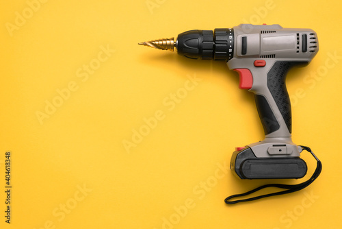 Screwdriver drill with step conical drill bit on the yellow flat lay background with copy space.