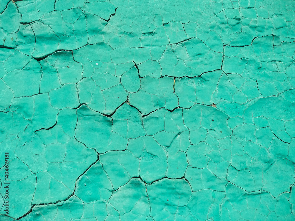 Close-up old green cracked paint. The texture of the old emerald paint with cracks. Dried in the sun and cracked color on the wall of country house. Peeling coating.
