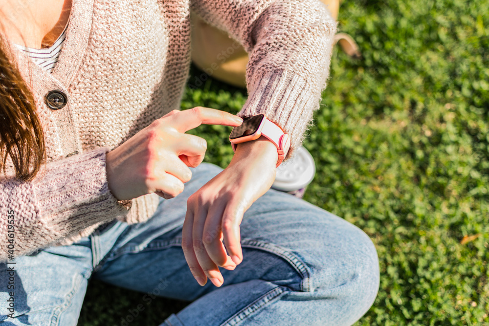 Close up of woman's hands checks the time on smart watch sitting in a park