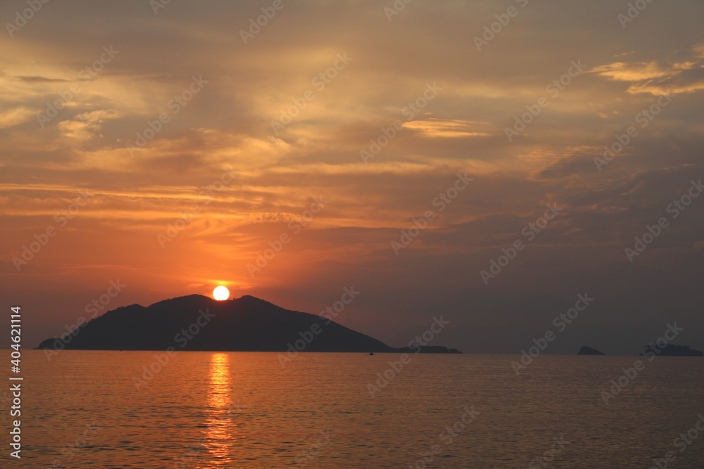 Colorful clouds, sunset, sea and island silhouettes. Orange sun on the hill.