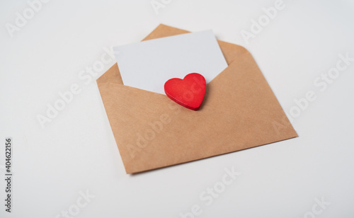 Craft envelope with a blank sheet of paper inside and red heart on the white background. Romantic love letter for the Valentine's day concept. Space for text.