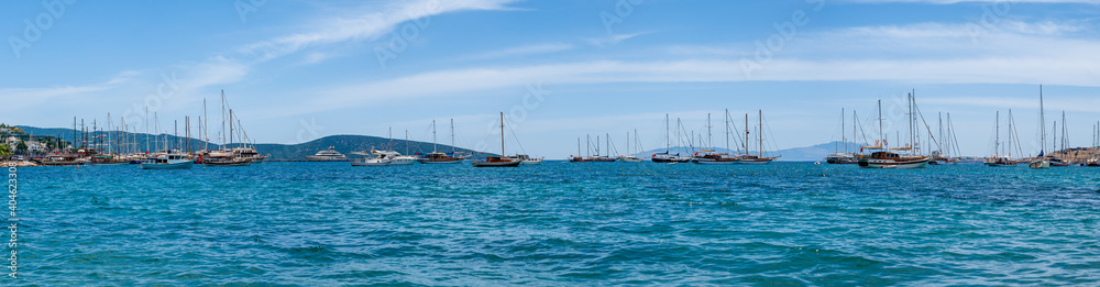 Panoramic distant view at yachts and sail boats anchored in calm waters of Bodrum shallow moon-shaped bay in Turkey.