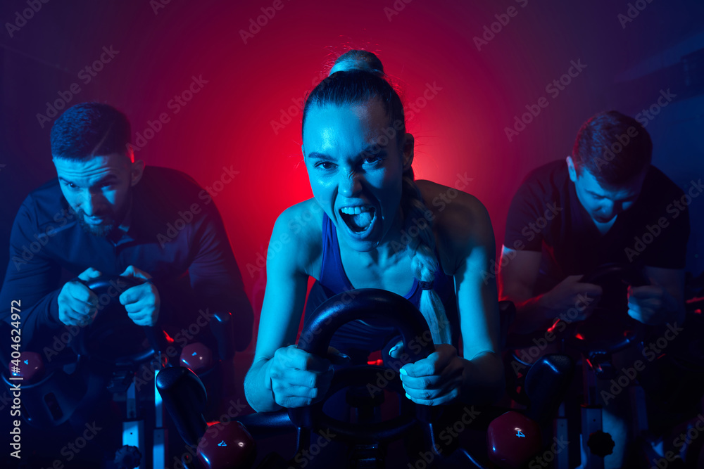 exercise bike cardio workout at fitness gym of woman and friends having intensive training, taking weight loss with machine aerobic for slim body, they are screaming