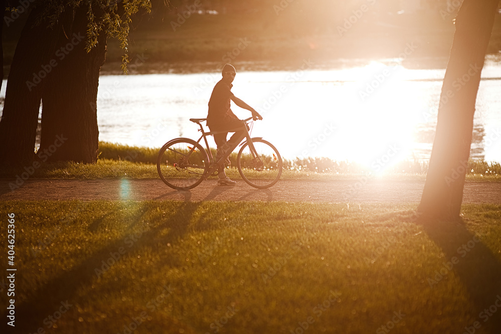 Obraz premium healthy young man rides a Bicycle, enjoying nature and sun. A free traveler travels with a bicycle at sunset. concept of adventure and travel. lonely cyclist resting in park.