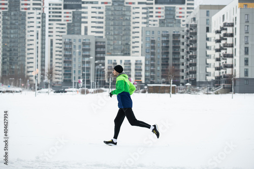 Man athlete running in winter cold. Training during Covid-19 pandemic. Winter exercise to stay fit. Urban city jogger. Smiling man fitness workout. Active and healthy life in quarantine atletico