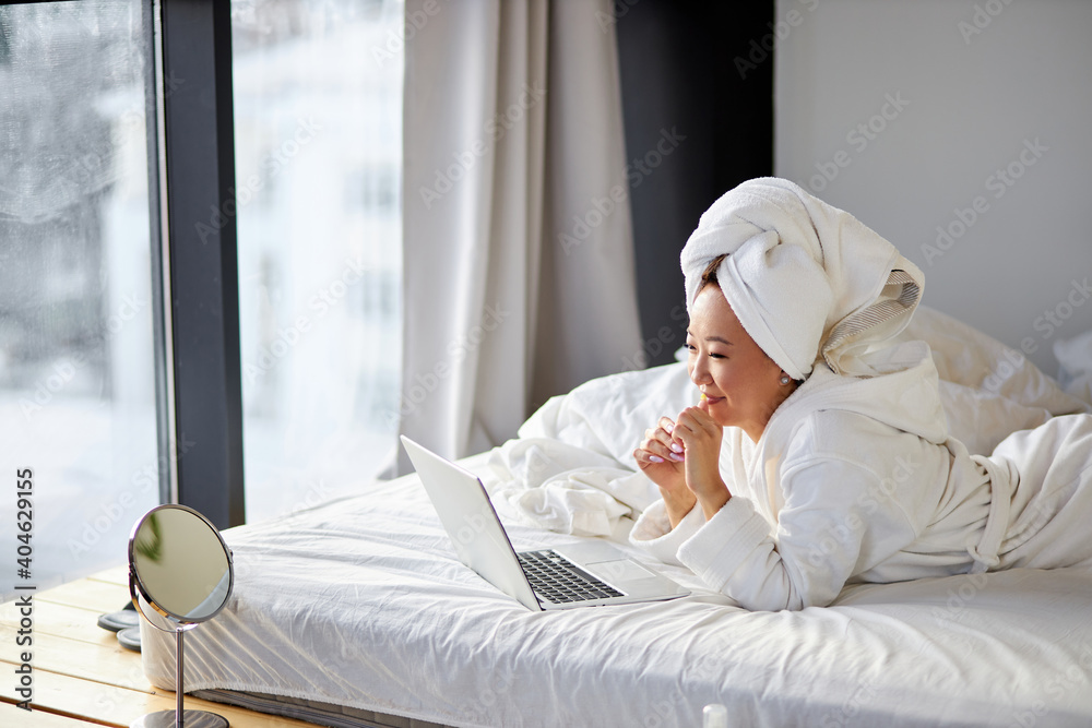 asian female looks at screen of laptop talking, smiling, have online conversation with someone, at home on bed asian female looks at screen of laptop talking, smiling, have online conversation with someone, at home on bed