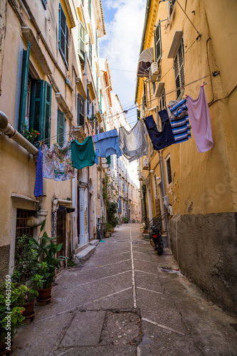 Old narrow street, old residential buildings and washed clothes on a rope in Kerkira, capital of Corfu island, Greece, hot summer day, blue sky. © sunday_morning