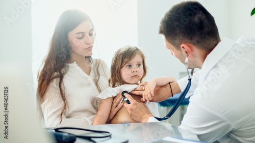 Male Doctor Pediatrician Using Stethoscope Listen to the Heart of Happy Healthy Cute Kid Girl at Medical Visit With Mother in the Hospital. Mother With Kid at Visiting Pediatrician.