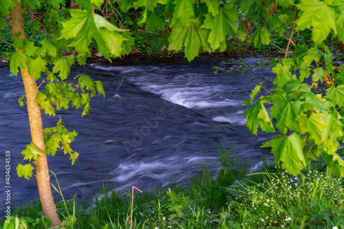 Blau grauer Flusslauf umrandet von grünen Blättern. Verschwommenes Wasser