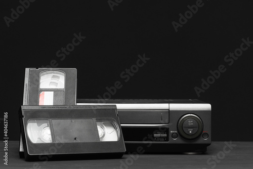 Video recorder and video tapes on the table on the black background.