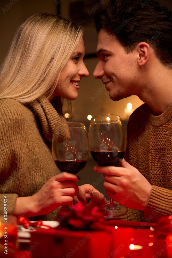 Happy young couple in love bonding, holding glasses, drinking wine, enjoy tender moment together celebrating Valentines day having romantic dinner date with candles sit at home table or in restaurant. - obrazy, fototapety, plakaty 