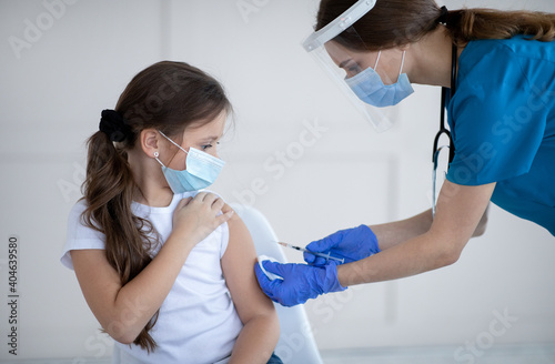 Covid-19 vaccination. Little girl in protective mask receiving coronavirus vaccine injection from doctor at clinic