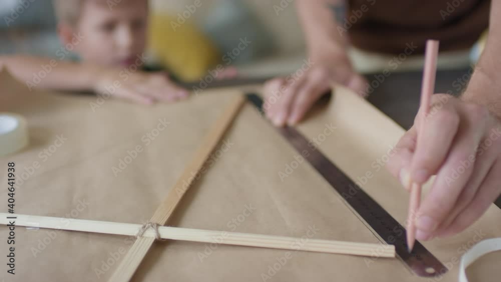 From-above close-up of unrecognizable man drawing outline while crafting diy kite and little boy watching process From-above close-up of unrecognizable man drawing outline while crafting diy kite and little boy watching process