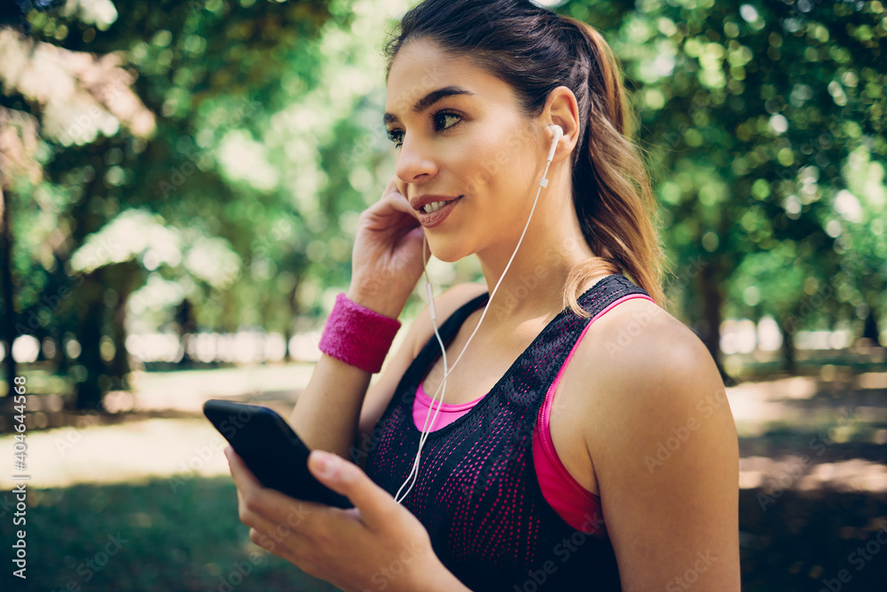 Portrait of female runner standing in nature and putting earphones in ears. Portrait of female runner standing in nature and putting earphones in ears.