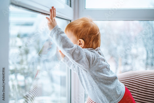the kid carefully looks out the window at the snow and what is happening around, side view, close-up with space for text.