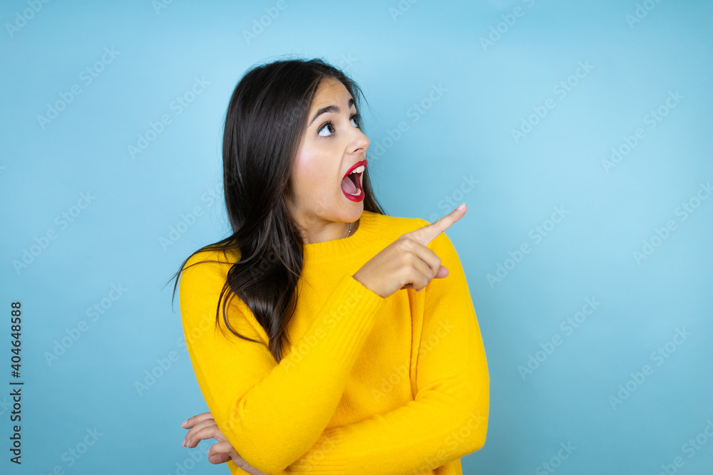 Young beautiful woman wearing yellow sweater over isolated blue background smiling and pointing with hand and finger to the side Young beautiful woman wearing yellow sweater over isolated blue background smiling and pointing with hand and finger to the side