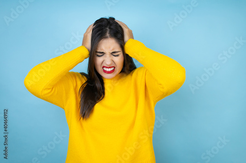 Young beautiful woman wearing yellow sweater over isolated blue background suffering from headache desperate and stressed because pain and migraine with her hands on head © Irene