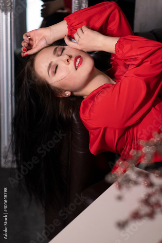 portrait of attractive brunette woman in red blouse lying on leather couch. st valentines.