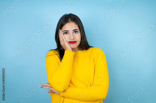 Young beautiful woman wearing yellow sweater over isolated blue background thinking looking tired and bored with crossed arms