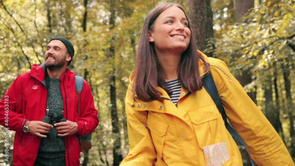 Two happy tourists walk in woods and enjoy nature. Beautiful caucasian girl looks around smiling while guy looks through binoculars. Two happy tourists walk in woods and enjoy nature. Beautiful caucasian girl looks around smiling while guy looks through binoculars.