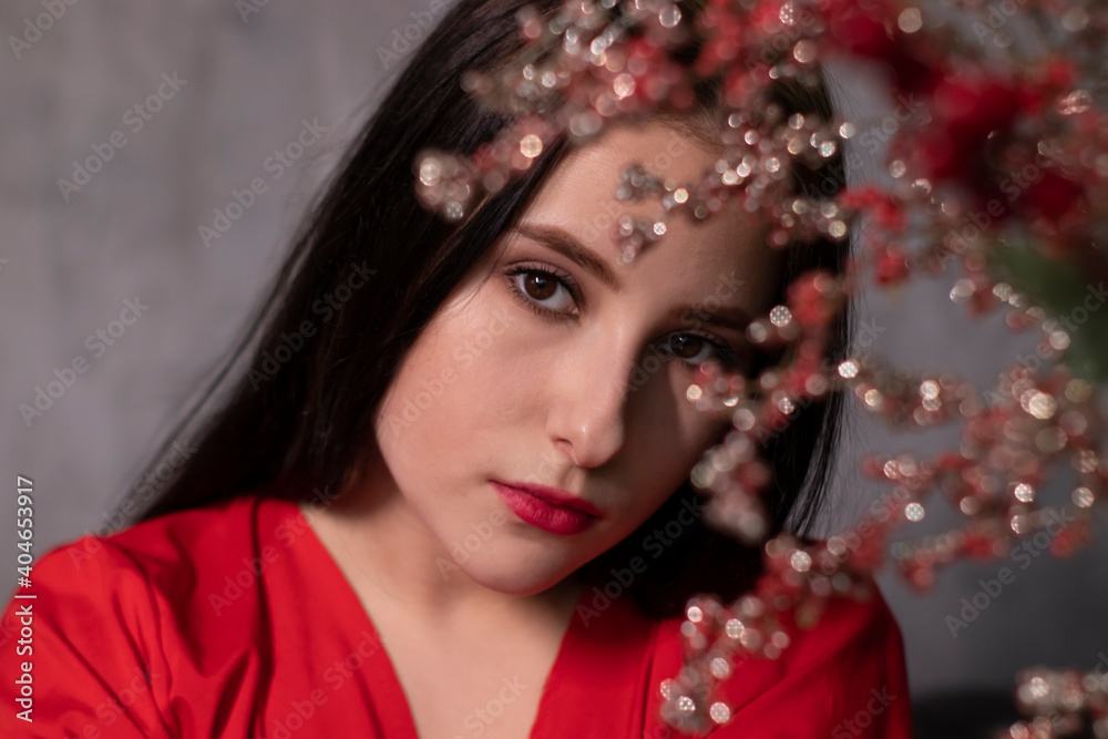 portrait of attractive brunette woman in red blouse near decorative sparkling red branches boquet. st valentines